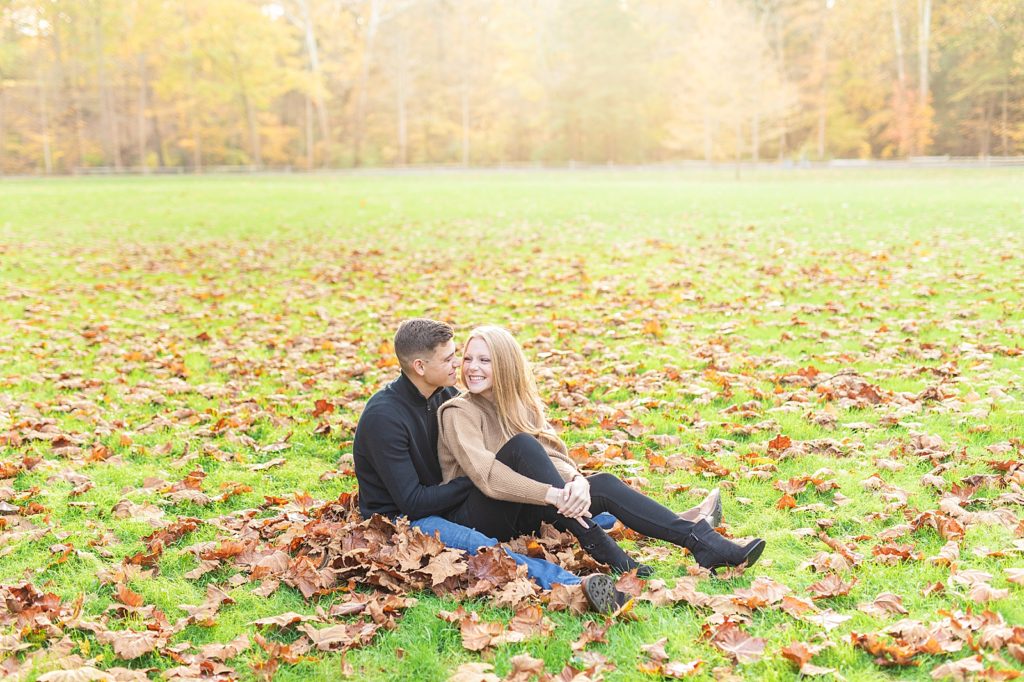 Engaged couple sitting in leaf pile in the woods.