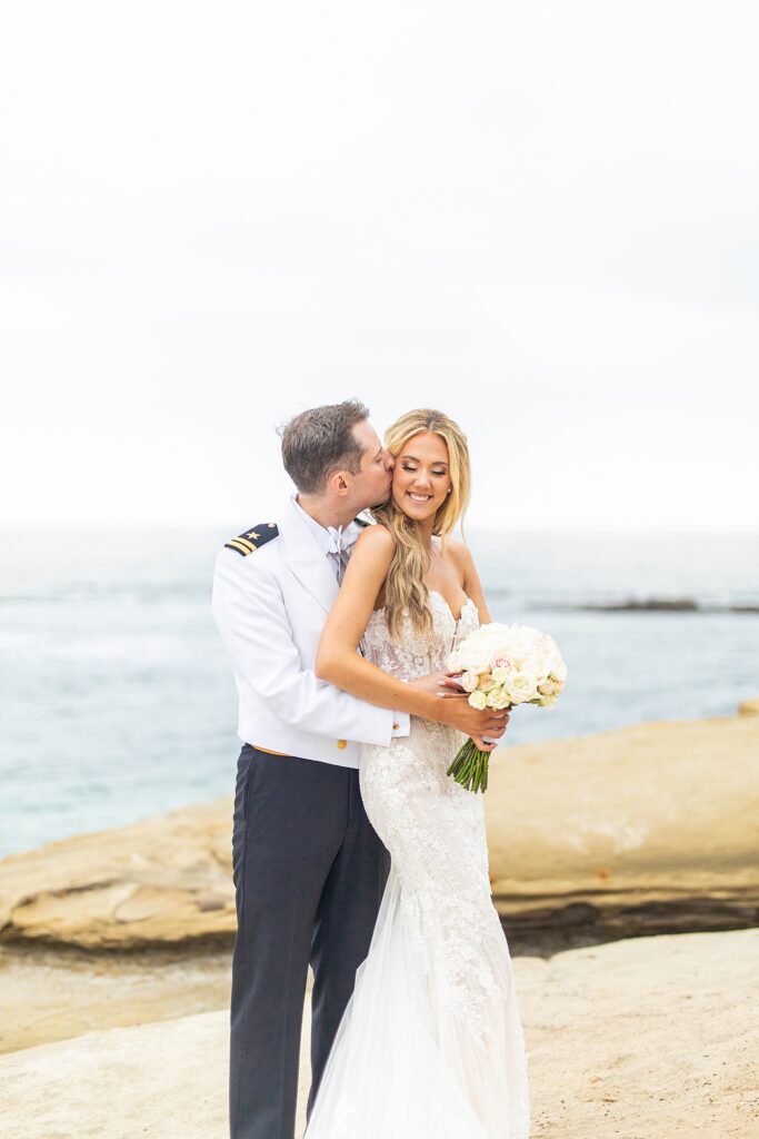 Groom kissing bride on the cliffs of La Jolla Beach.