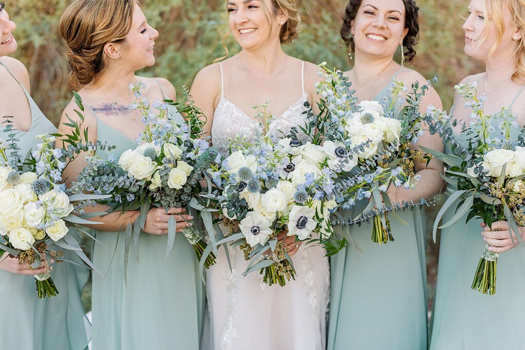 Bride with bridesmaids in Birdy Grey sage dresses with their bouquets.