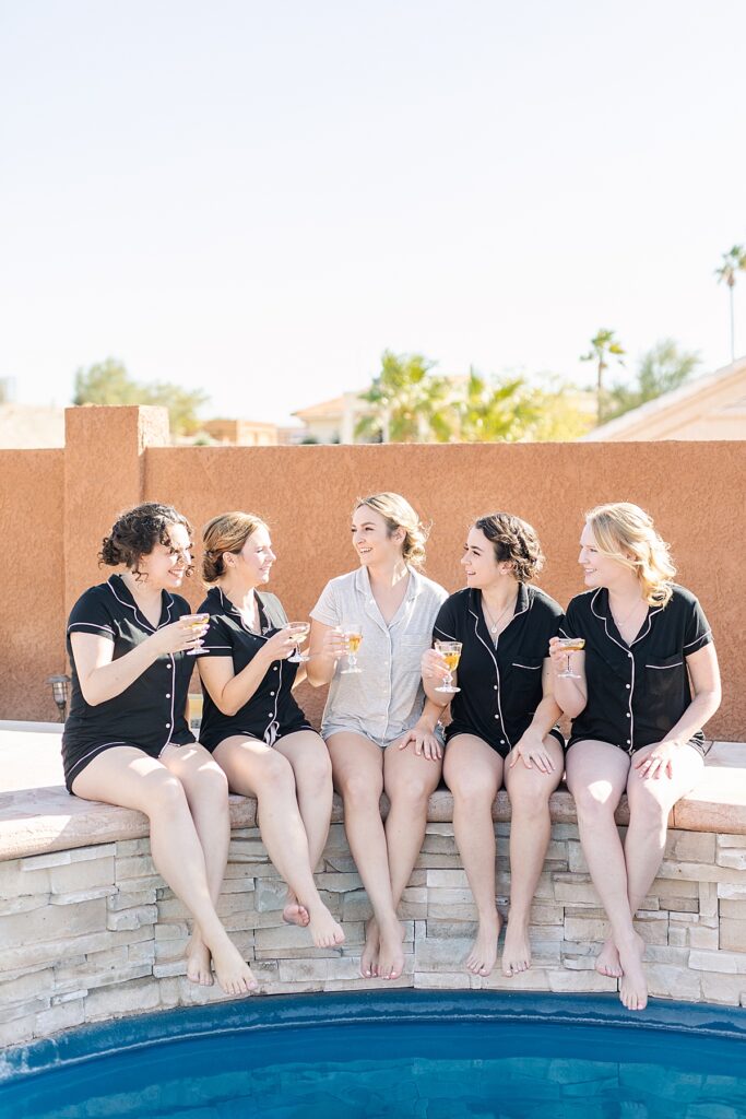 Bride and bridesmaids sitting by the pool sipping champagne.