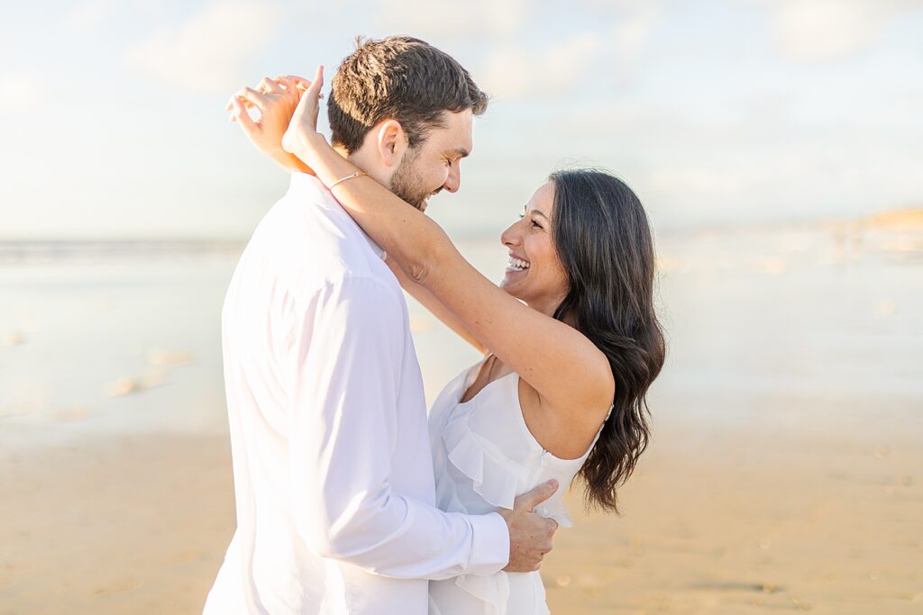 Bride in ruffle white dress and groom in white button down and khaki pants kissing overlooking the ocean in Del Mar, California.