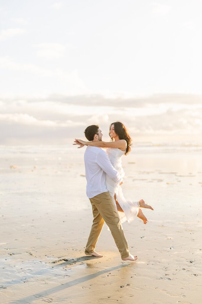 Engaged couple running on the beach during sunset.