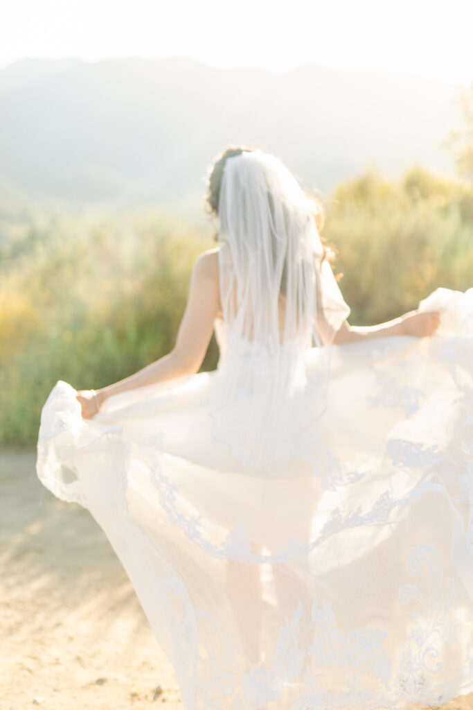 Candid image of bride running away from the camera in her veil and gown, her train flowing in the wind behind her in Costa Mesa, California.