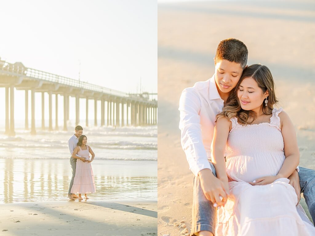 A couple in a pink ruffled maternity dress and a white button-down shirt pose together by Scripps Pier in La Jolla, with the beach and soft golden hour lighting in the background.