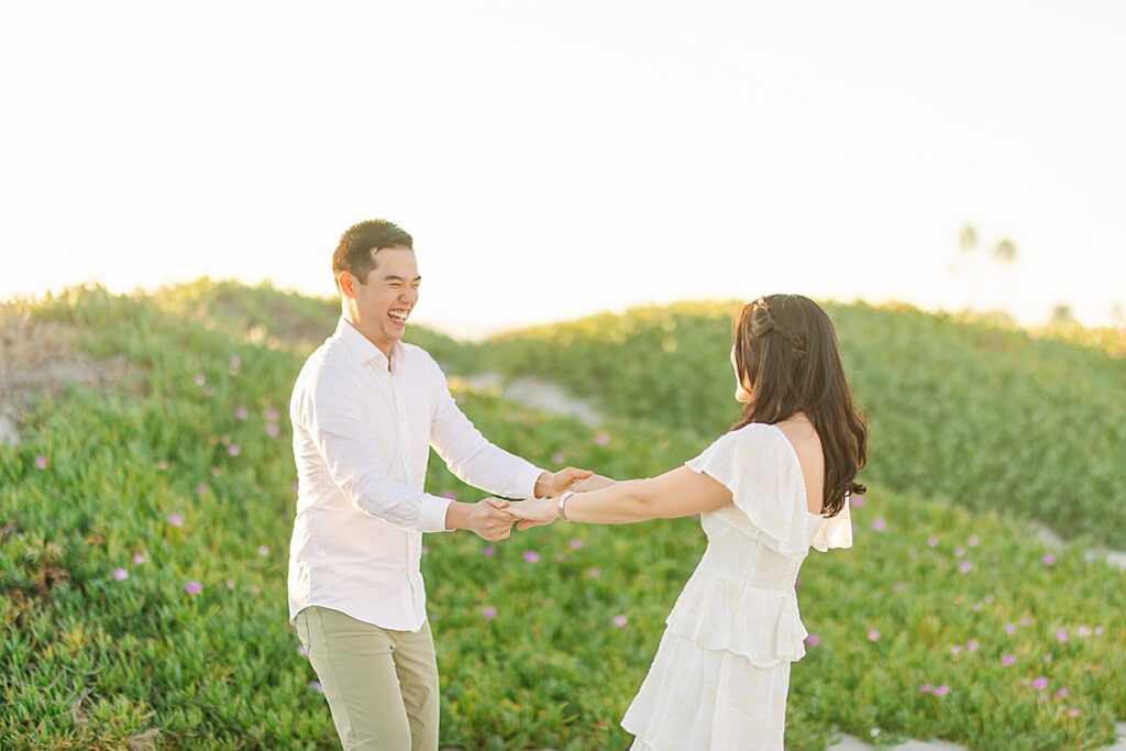Couple laughing together and dancing during their beach engagement session at Coronado Beach in San Diego, California.