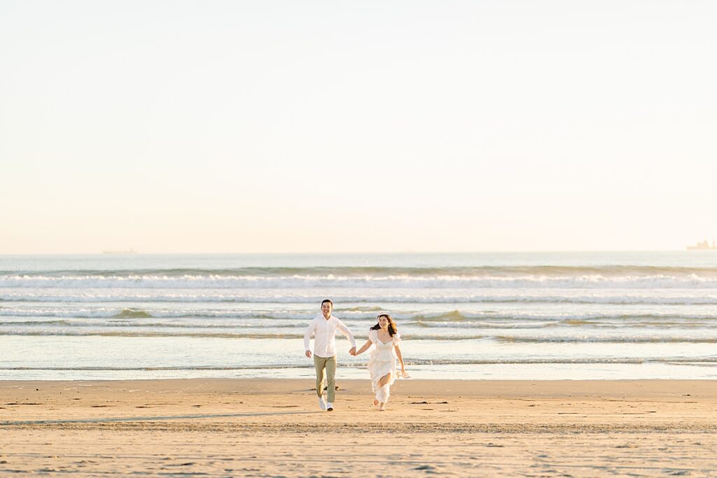 Couple running up the beach together in San Diego dressed in neutrals.