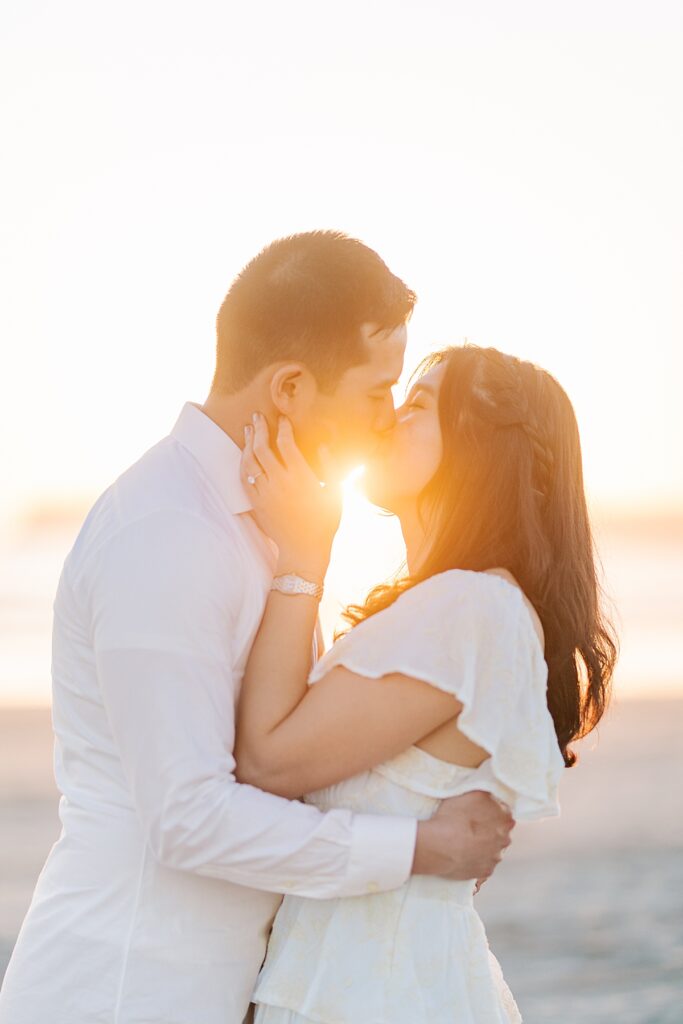 Jiaqi and Eric stand together on the beach, bathed in soft golden light, gazing lovingly at each other as the waves gently crash in the background.