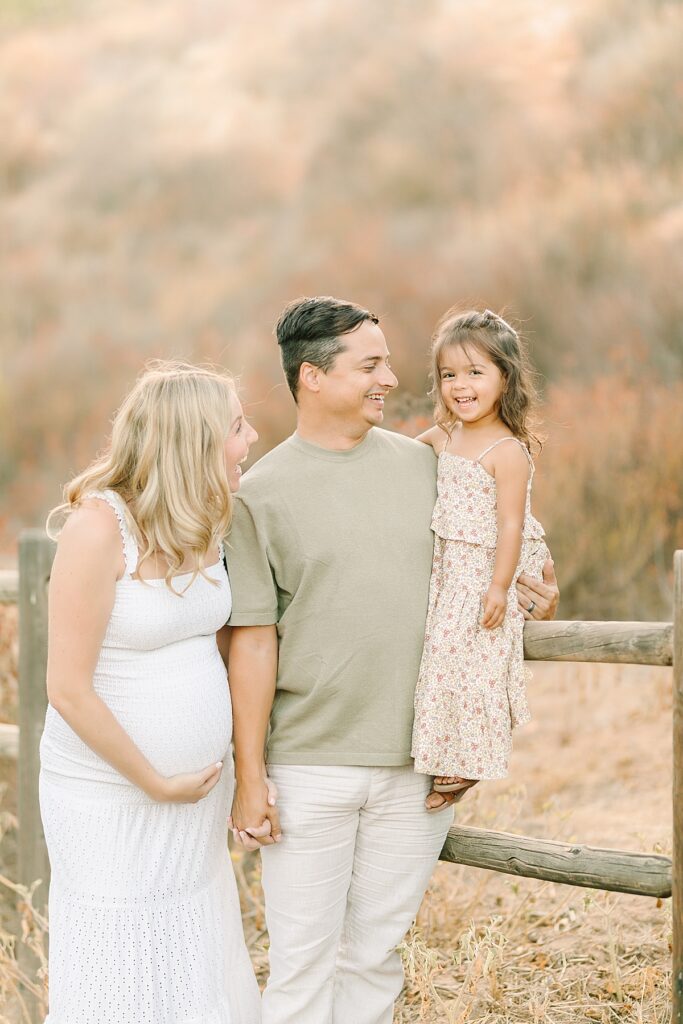 Family of three laughing together in a wide-open field with rolling hills at Mission Trails maternity session.