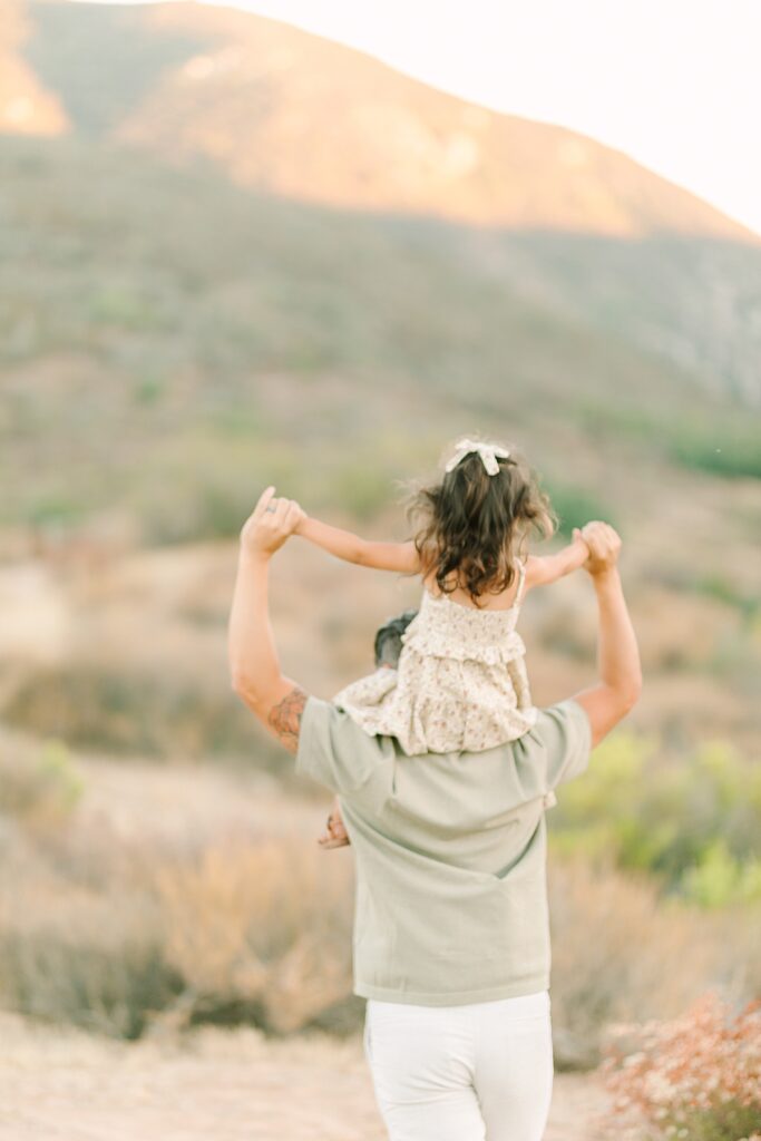 Dad holding toddler daughter on his shoulders, hills in the background at Mission Trails Maternity Session.