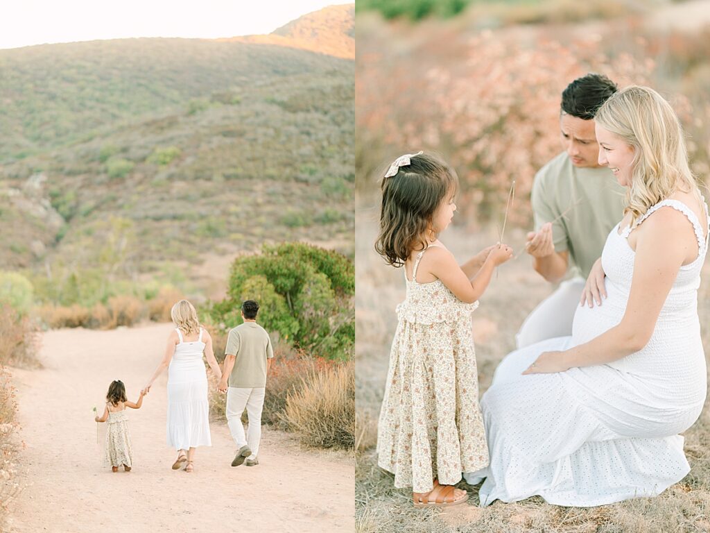 Mom and dad walking hand in hand with their toddler daughter on a dirt trail, all dressed in neutral tones.