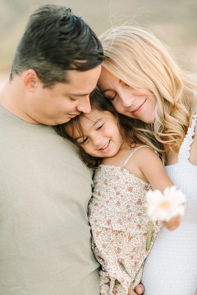 Family of three snuggled together in a wide-open field with rolling hills at Mission Trails.
