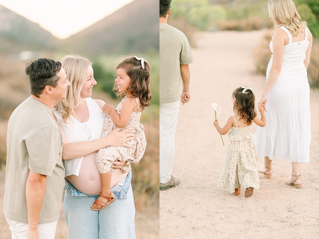 Mom and dad walking hand in hand with their toddler daughter on a dirt trail, all dressed in neutral tones.