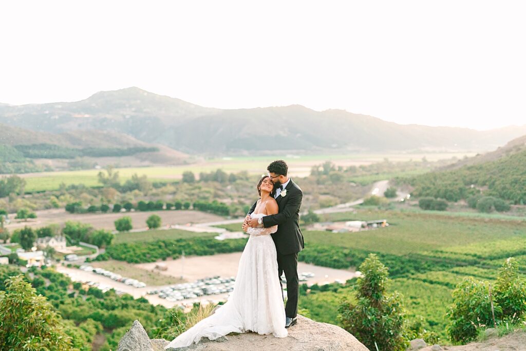 Groom kissing bride on the cheek at the Eagle's Nest overlook at Rancho Guejito Vineyard in Escondido.