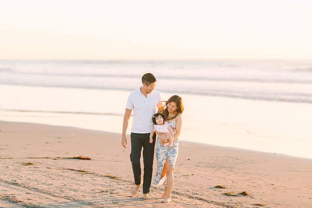 Small family walking away from the ocean on the sandy beach in San Diego.